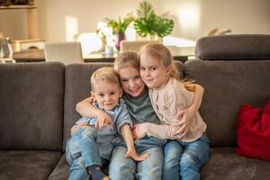 portrait of three children at home. brother and sisters sit on the couch hugging and smiling photo