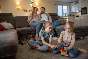 children, sisters have fun playing on the floor at home while parents are relaxing on the sofa photo