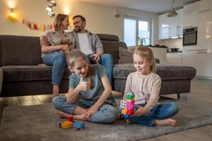 children, sisters have fun playing on the floor at home while parents are relaxing on the sofa photo