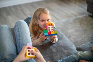 kids are playing with blocks. The boy sits on the sofa and builds a house from the constructor photo