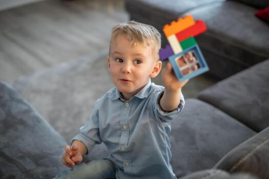 A small child plays with blocks. The boy sits on the sofa and builds a house from the constructor photo