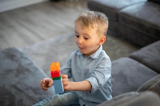 A small child plays with blocks. The boy sits on the sofa and builds a house from the constructor photo