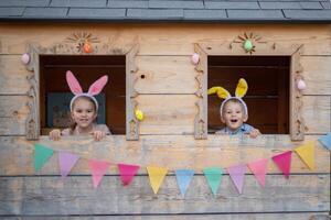 cute cheerful kids in bunny ears in the playhouse celebrate easter. brother and sister looking out the window photo