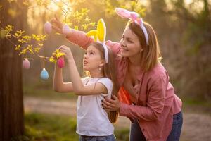 beautiful and happy mom and daughter in bunny ears decorate the tree with easter eggs. happy family celebrating easter photo