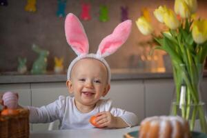 happy cute little baby girl wearing bunny ears on easter day sitting at the table in the kitchen photo