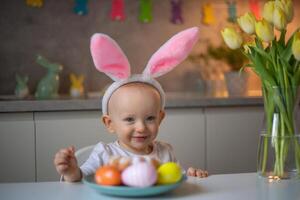 happy cute little baby girl wearing bunny ears on easter day sitting at the table in the kitchen photo