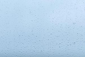 Raindrops collecting on a window during a gloomy day, creating a blurred view of the overcast sky outside photo