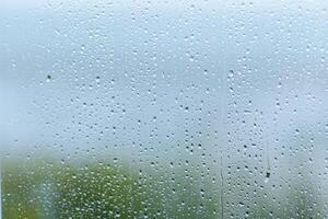 Rainy day with droplets on a windowpane, creating a blurred view of greenery outside during overcast weather photo