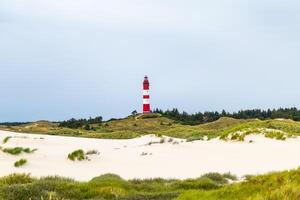 Red and white lighthouse standing tall in the sandy dunes under an overcast sky at the coastline photo