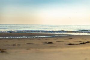Waves gently lap on the sandy shore under a clear sky during the early evening at a tranquil beach photo