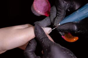 Technician in black gloves using tool for precise treatment of client's nail. photo