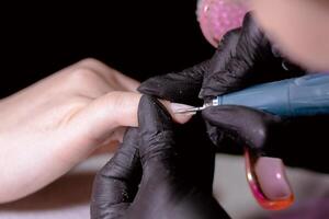 Manicure process. Technician in black gloves using tool on client's nails. photo