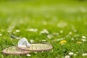 Two badminton rackets and a shuttlecock lie on the green grass. photo