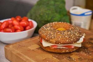 Close-up of breakfast bagel with cheese, tomato and fried egg inside. Tasty sandwich made from sesame and poppy seed bagel on wooden board photo