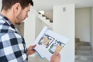 Man analyzing architectural blueprint in new apartment photo
