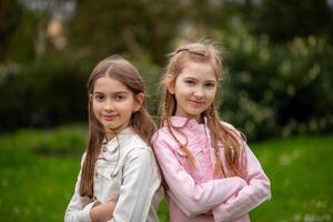 Two charming girls in pastel-shaded outfits, smiling amiably and posing in a green spring park. photo