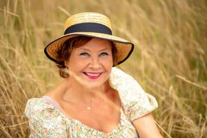 Woman wearing a straw hat smiling in a grassy field during daylight photo