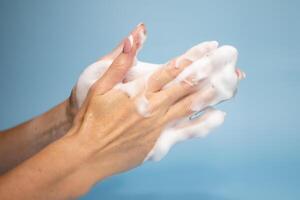 Woman washing hands with soap on color background photo