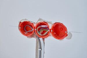 Electrical wiring installation during renovation. Three plastic outlet boxes with exposed electrical wires embedded in wall. Unfinished wall with visible electrical wiring and socket holders photo
