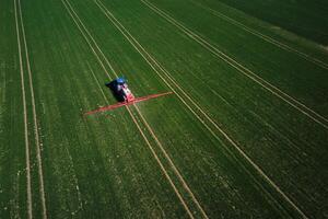 Tractor working in agricultural field, aerial view. Tractor spraying crop field with fertilize or pesticide for good harvest. Concept of farming technology and crop care photo
