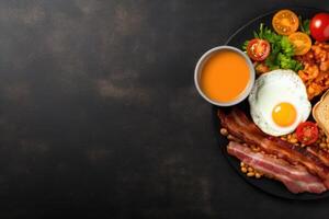 English breakfast on a plate with scrambled eggs, sausages, bacon, beans, toast and coffee on a dark stone background. photo