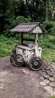 Two bicycles leaning against an old wooden well in the middle of a green forest. Peaceful summer scene with natural textures, trees, and tranquil atmosphere. photo