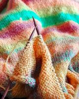Bright and cozy photo of hand knitting in progress using multicolored yarn and wooden needles. Ideal for DIY, crafting, textile design, and handmade lifestyle visuals.