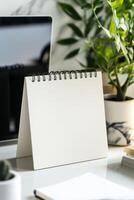 Desk setup with blank notepad and green plants in a modern workspace during the daytime photo