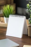 Blank spiral notebook on a wooden desk surrounded by plants during daytime at a cozy workspace photo