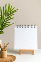 Blank notepad on stand with plant and stationery on a light-colored table in a cozy workspace setting photo