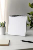 Blank notebook on a desk beside plant with stationery in soft natural light photo