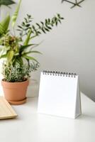 Blank table calendar placed on a work desk surrounded by indoor plants in a cozy workspace setting photo