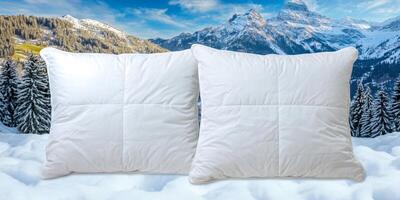 Cozy white pillows placed on snow with a stunning mountain backdrop surrounded by evergreen trees under a clear sky photo