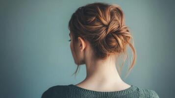 Woman with a stylish bun hairstyle poses against a simple blue background in natural light photo