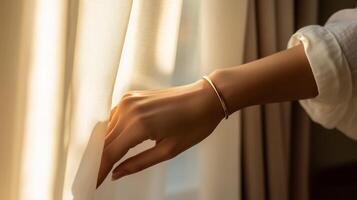 Soft morning light illuminates a hand gently drawing back sheer curtains in a cozy room photo