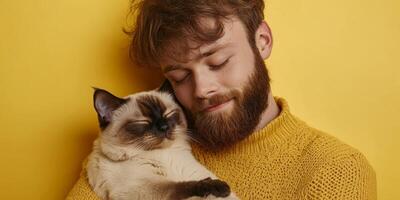 Young man enjoys a joyful moment with his content cat against a vibrant yellow background photo