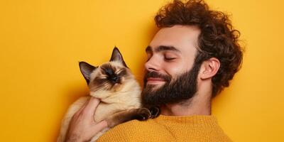 Man enjoys affectionate moment with playful cat against a vibrant yellow backdrop during a cozy indoor setting photo