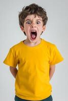 Young boy expresses intense emotion with a loud scream while wearing a bright yellow t-shirt against a plain background photo