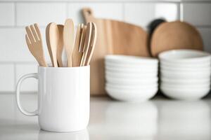 Wooden kitchen utensils arranged in a white mug on a countertop with bowls in the background photo