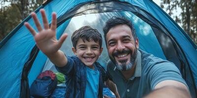 Father and son enjoy camping adventure together while taking a selfie in front of their tent photo