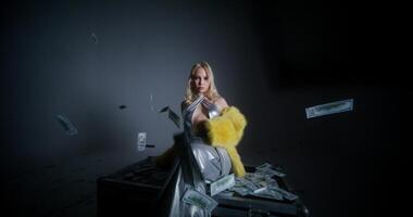 A woman in a yellow dress sitting on a suitcase with money falling from the sky photo