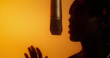 A person singing into a microphone in front of an orange background photo