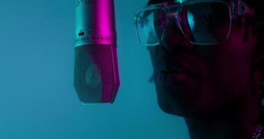 A man with glasses and a microphone in front of a blue background photo