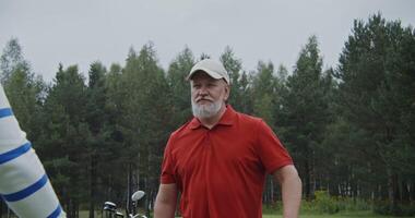 An elderly gray-haired man talks to another man while standing on a golf course photo