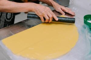 Hands rolling out yellow dough on a silver surface, preparing food photo