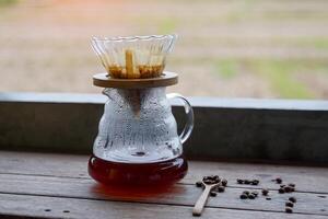 Black coffee in a glass pitcher of a coffee dripper set placed on a wooden counter. photo
