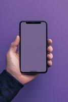 Hand holding smartphone with a blank screen against a solid purple background showcasing modern minimalism photo