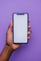 Hand holding a smartphone against a purple background, showcasing a blank screen for creative content photo