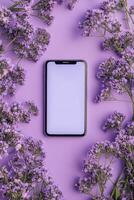 Smartphone surrounded by purple flowers on a pastel background during daytime photo