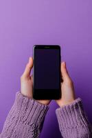 Hands holding a black smartphone against a vibrant purple background in a cozy indoor setting photo